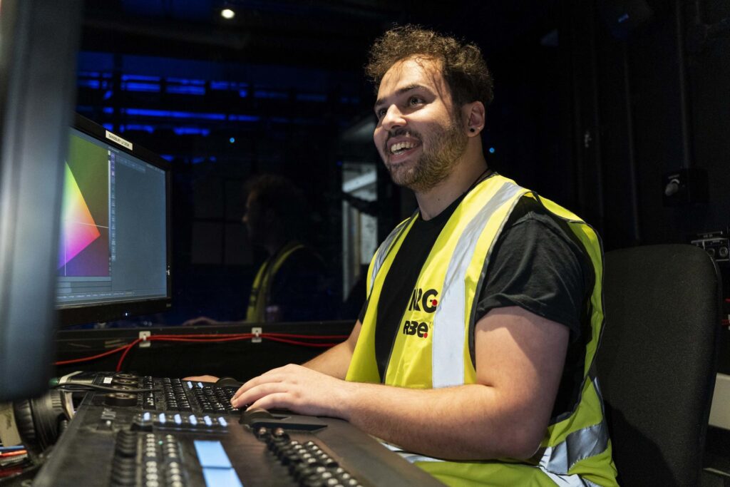Man in a hi-vis vest smiling while operating a lighting control desk with a colour-mapping screen